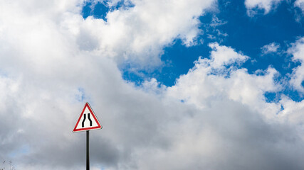 Isolated traffic sign indicating a warning on a dramatic sky, with dark clouds and blue sky.