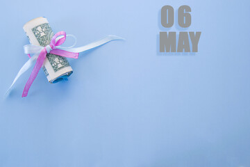 calendar date on blue background with rolled up dollar bills pinned by blue and pink ribbon with copy space.  May 6 is the sixth day of the month