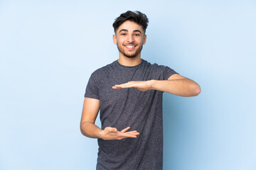 Arabian handsome man over isolated background holding copyspace imaginary on the palm to insert an...