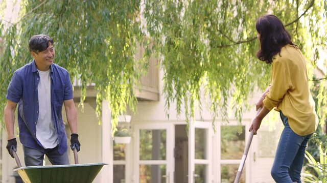 Mature Asian couple working in garden at home raking leaves into barrow- shot in slow motion