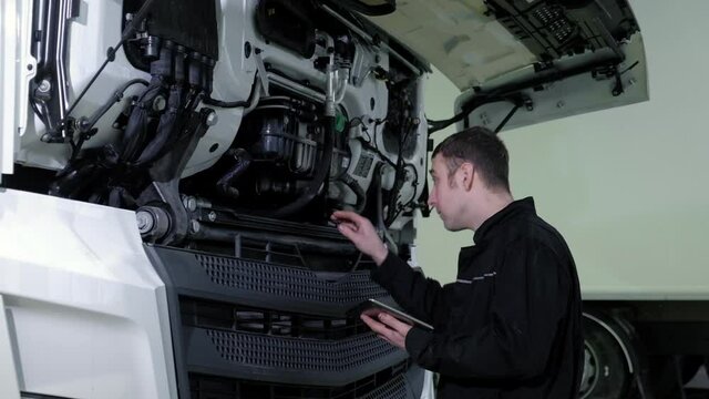 Repair diagnostics and maintenance of cars in service center. chief mechanical engineer in uniform stands next to truck uses tablet to search for errors and breakdowns and writes data to the computer