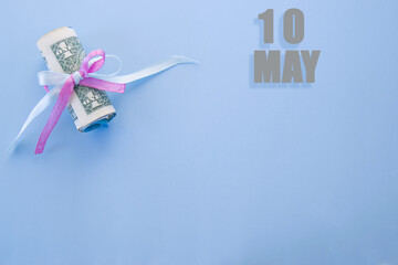 calendar date on blue background with rolled up dollar bills pinned by blue and pink ribbon with copy space. May 10 is the tenth day of the month