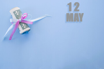 calendar date on blue background with rolled up dollar bills pinned by blue and pink ribbon with copy space. May 12 is the twelfth day of the month