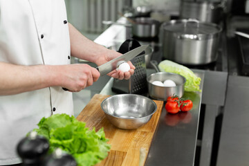 Cook breaks an egg. Egg yolk falling into the bowl