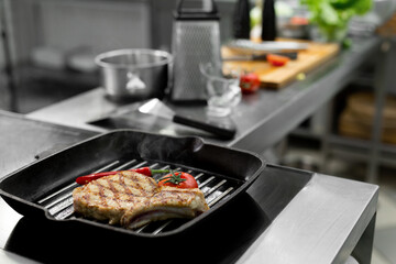 Close-up of a chef's hand holding a grill pan with grilled steaks and vegetables