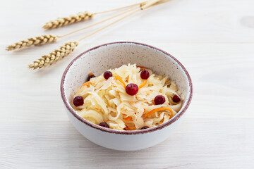 Pickled cabbage with cranberries in a bowl on a background of wheat on a white table.