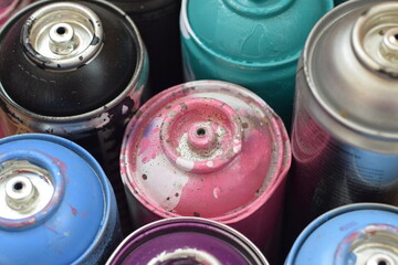 Large number of used colorful spray cans of aerosol paint lying on the treated wooden surface in...