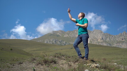 A young man is looking for a cellular network in the Caucasus Mountains. The man is talking on the...