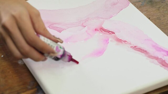 Close up of female artist paints an abstract picture, he uses pink paint fron tube on wet canves