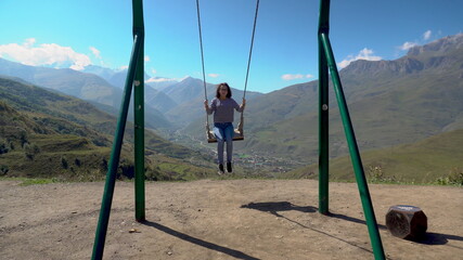 Young woman goes for a drive on a swing against a background of Caucasian mountains.