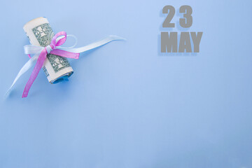 calendar date on blue background with rolled up dollar bills pinned by blue and pink ribbon with copy space. May 23 is the twenty-third  day of the month