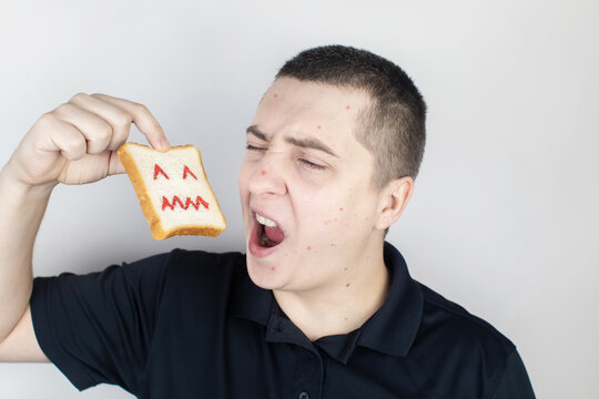 Conceptually about gluten intolerance. The man holds in his hand a piece of bread on which an angry expression is painted. Celiac disease, fear of cereals, manifestation of allergies