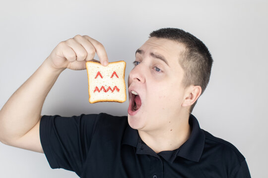 Conceptually about gluten intolerance. The man holds in his hand a piece of bread on which an angry expression is painted. Celiac disease, fear of cereals, manifestation of allergies