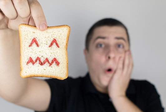 Conceptually about gluten intolerance. The man holds in his hand a piece of bread on which an angry expression is painted. Celiac disease, fear of cereals, manifestation of allergies