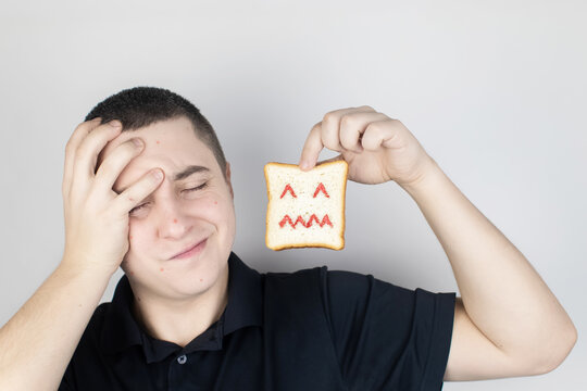 Conceptually about gluten intolerance. The man holds in his hand a piece of bread on which an angry expression is painted. Celiac disease, fear of cereals, manifestation of allergies