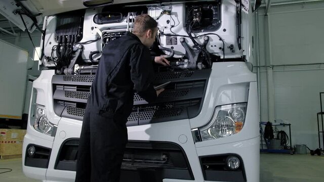 Repair diagnostics and maintenance of cars in service center. mechanic engineer of car service inspects transport cargo uses tablet to search for errors and breakdowns and writes data to the computer