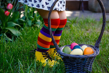 Close-up of legs of toddler girl with colorful stockings and shoes and basket with colored eggs....