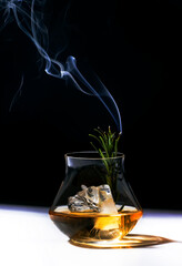 Contemporary still life with whiskey, scotch or bourbon glass with steaming rosemary, shard ice on black white background