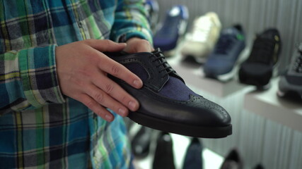 A young man holds a shoe in his hand and touches it in the store. Shoe store.