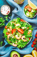 Fresh shrimp salad with tomatoes, lettuce, arugula, avocado, cucumber and lemon dressing on white background. Healthy eating, clean food concept. Top view