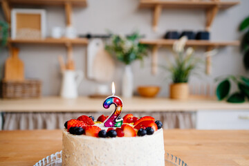 cake with candle number two and fruit on table on kitchen 