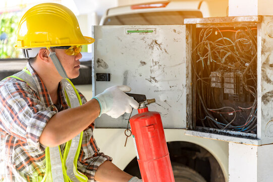 Electrician using a fire extinguisher to put out an electrical fire, Thailand
