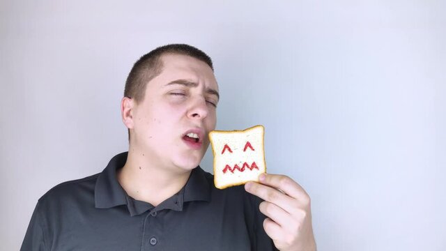 Conceptually about gluten intolerance. The man holds in his hand a piece of bread on which an angry expression is painted. Celiac disease, fear of cereals, manifestation of allergies