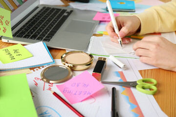Woman writing at messy table, closeup. Concept of being overwhelmed by work