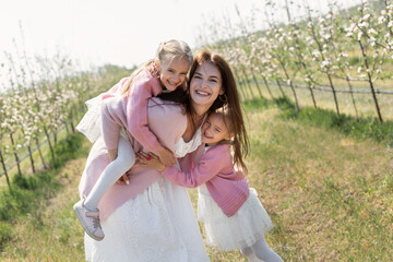 Fototapeta na wymiar Happy family in the Apple orchard. Mom and two twin daughters have fun and hug