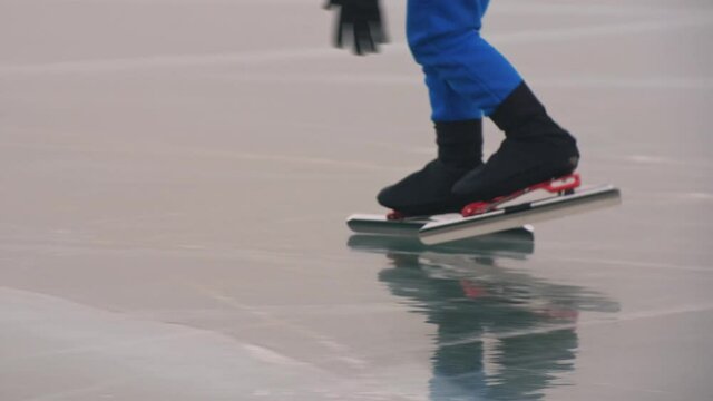 The child train on ice speed skating. The legs in skates close up. The kid girl skates in the winter in sportswear, sport glasses. Children speed skating short long track. Outdoor slow motion.