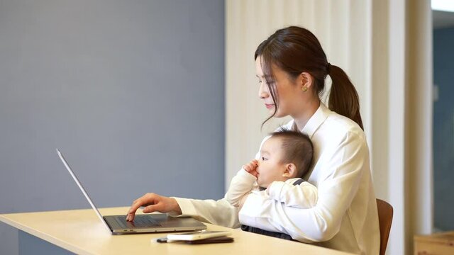 赤ちゃんを抱えてノートパソコンを操作する女性
