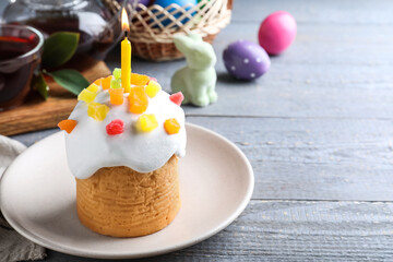 Traditional Easter cake with burning candle on grey wooden table. Space for text