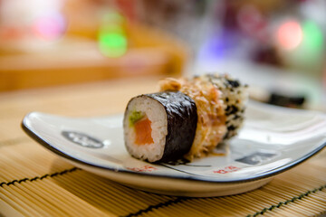Three sushi on a white plate standing on a bamboo tablecloth
