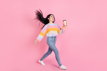 Full size profile side photo of young funky smiling girl go walk with flying hair drink tea isolated on pink color background