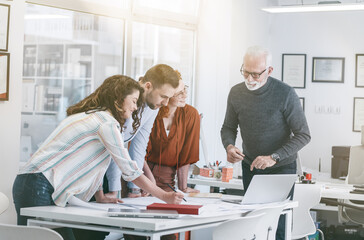 Obraz premium Working day in a design studio.Group of designers and architects discuss about new project.They sitting at the desk and looking at the blueprint.