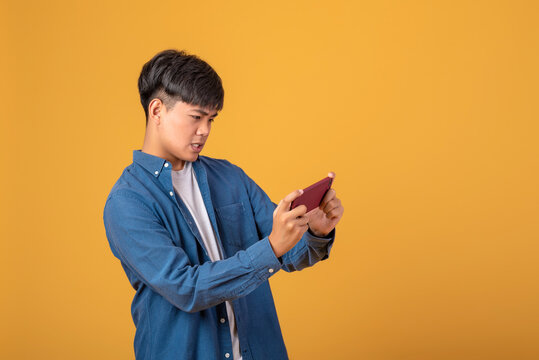 Image of a young Asian man is serious. With playing games via mobile phone. On orange background