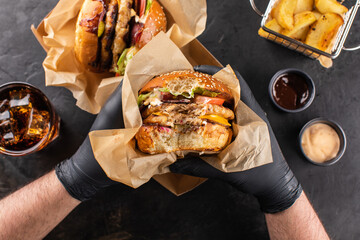 Yummy grilled chicken hamburger with a double cutlet in hand, ready to eat. Burger and French fries...