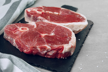 Raw rib-eye beef steak on wooden cutting board on gray background