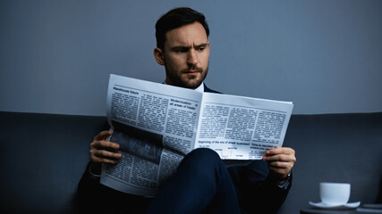 Focused businessman reading news near coffee on blurred foreground in hotel