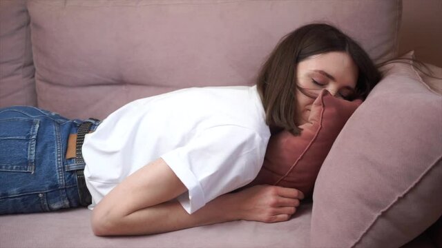 An exhausted, overwhelmed young woman in a white T-shirt came after work, plopping down on the sofa, looking like a squeezed lemon. Concept after party, tired, overworked person, hard day. Slow motion