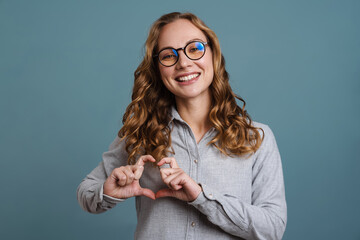 Happy girl in eyeglasses smiling and showing heart gesture
