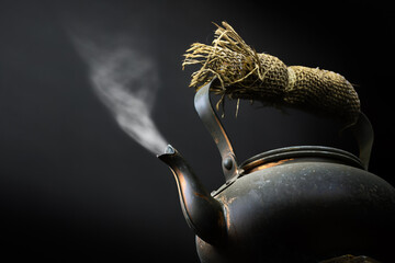 Black metal tea or coffee kettle close-up from a low angle with hot steam coming out the spout still life fine art. Stock - 417628371