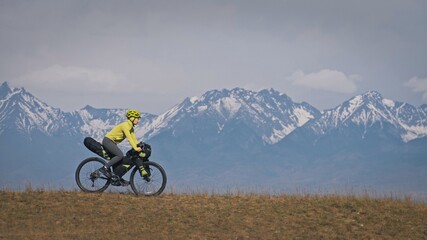 The woman travel on mixed terrain cycle touring with bikepacking. The traveler journey with bicycle bags. Sport tourism bikepacking, bike, sportswear in green black colors. Mountain snow capped. © ivandanru