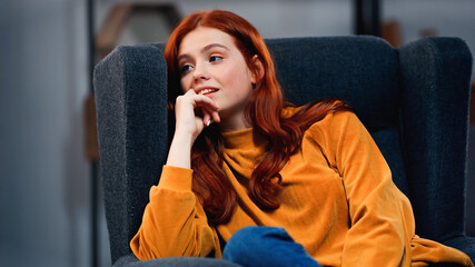 Smiling red haired teenager sitting on armchair at home