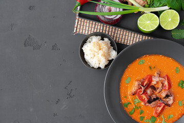 Tom yam Thai soup in black bowl served on gray background
