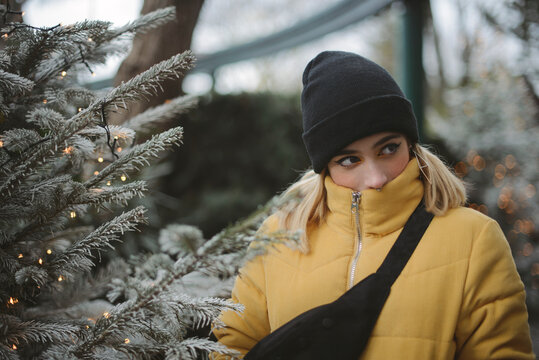 Portrait of a young woman in a puffer jacket standing by a Christmas tree, France
