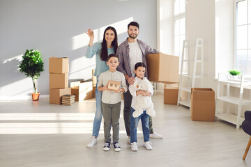 Fototapeta na wymiar Young happy family with children boy and girl standing together and holding boxes with belongings in new spacious apartment after relocating. Renting buying or moving to new accomodation concept