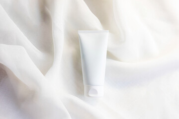 white cosmetic tube for face cream, cleanser, body lotion or shampoo on white draped cloth. Gentle skin care concept. Copy space