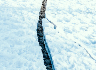 Large crack in permafrost ice revealing dry rocks hidden beneath.