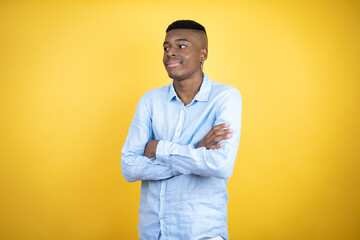 Young african american man wearing a casual shirt standing over yellow background looking to the side with arms crossed convinced and confident